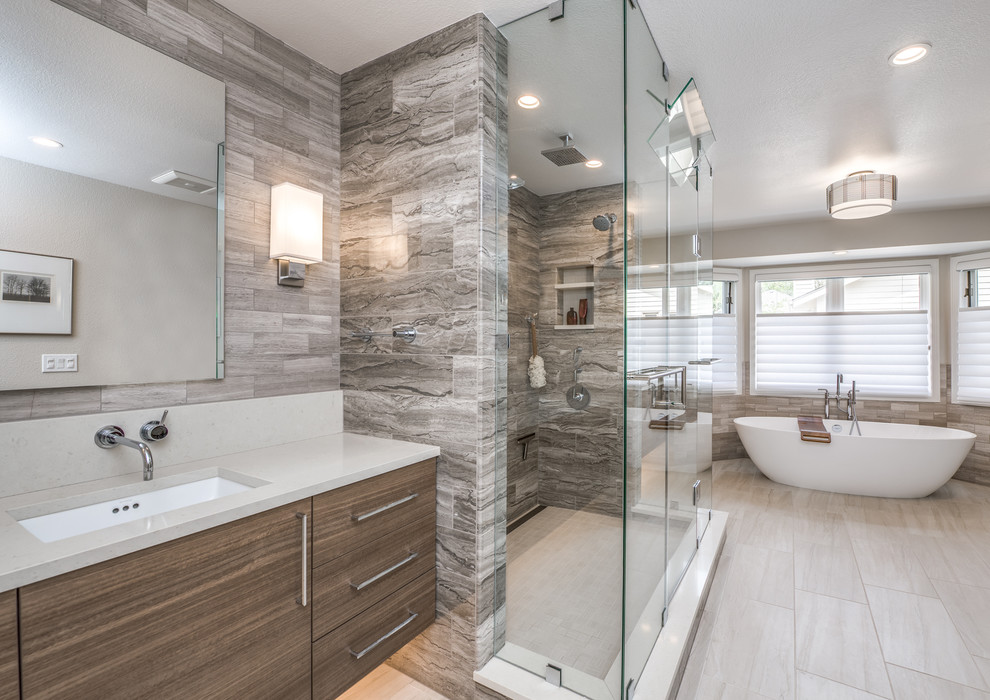 Design ideas for a large contemporary master bathroom in Denver with flat-panel cabinets, light wood cabinets, a freestanding tub, a double shower, a wall-mount toilet, beige tile, limestone, grey walls, porcelain floors, an undermount sink, engineered quartz benchtops, white floor, a hinged shower door and white benchtops.