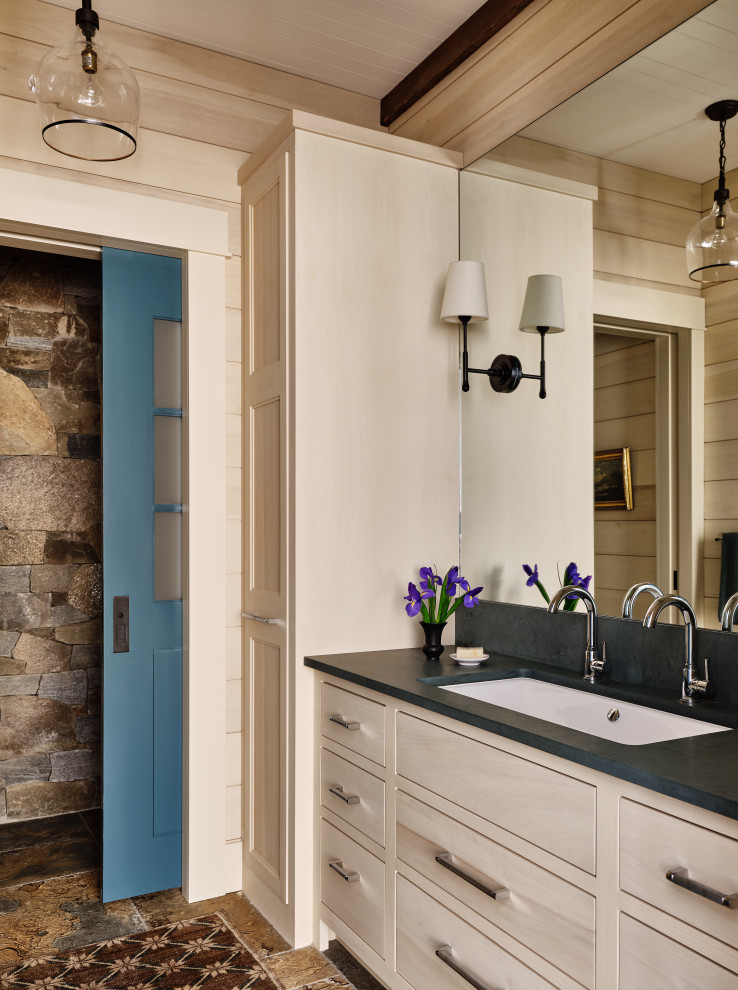 Photo of a country bathroom in Burlington with flat-panel cabinets, light wood cabinets, beige walls, a trough sink, brown floor, black benchtops, an enclosed toilet, a double vanity, a built-in vanity and wood walls.