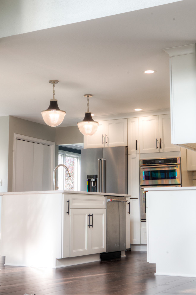 Inspiration for a large transitional l-shaped dark wood floor and brown floor home design remodel with an undermount sink, recessed-panel cabinets, white cabinets, quartz countertops, white backsplash, subway tile backsplash, stainless steel appliances and an island