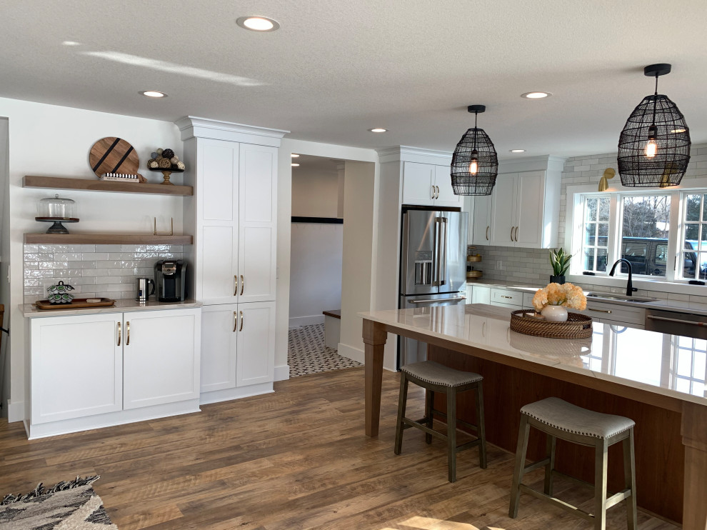 Example of a large transitional l-shaped vinyl floor and brown floor eat-in kitchen design with an undermount sink, shaker cabinets, white cabinets, quartz countertops, stainless steel appliances, an island and gray countertops