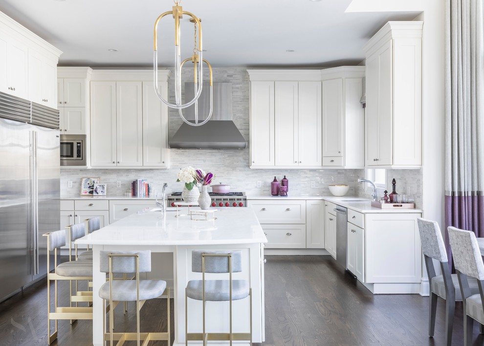 This is an example of a contemporary u-shaped eat-in kitchen in New York with an undermount sink, shaker cabinets, white cabinets, limestone splashback, stainless steel appliances, dark hardwood floors, with island, brown floor and white benchtop.
