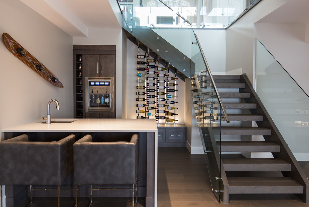 Photo of a mid-sized contemporary single-wall seated home bar in Calgary with an undermount sink, shaker cabinets, dark wood cabinets, quartz benchtops, medium hardwood floors and brown floor.