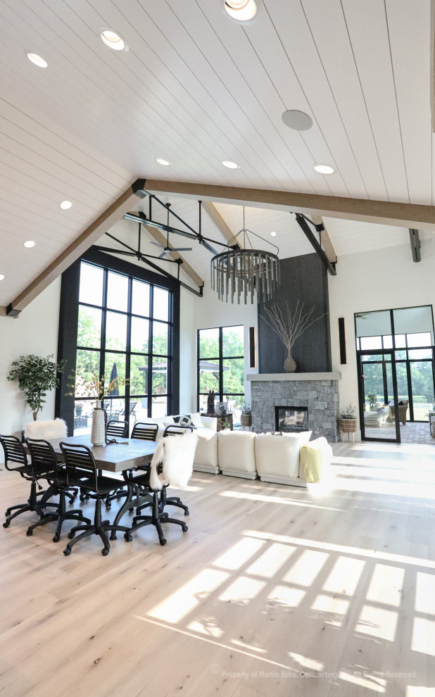 Photo of an expansive industrial open plan living room in Other with white walls, light hardwood flooring, a two-sided fireplace, a stacked stone fireplace surround, no tv and a vaulted ceiling.