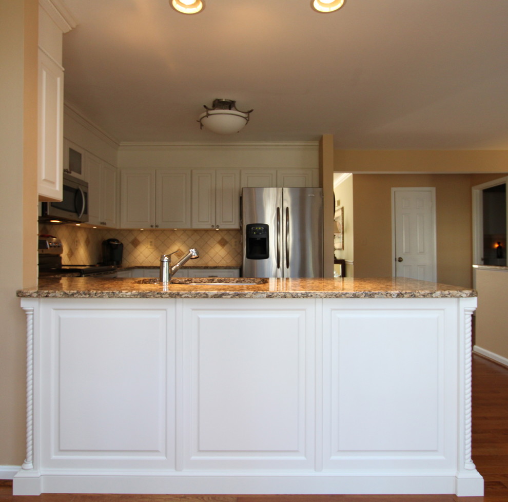 This is an example of a transitional u-shaped eat-in kitchen in Baltimore with an undermount sink, raised-panel cabinets, white cabinets, granite benchtops, stainless steel appliances, medium hardwood floors, a peninsula, beige splashback and ceramic splashback.