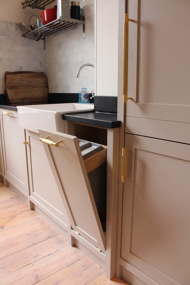 Inspiration for a large arts and crafts single-wall open plan kitchen in London with a farmhouse sink, shaker cabinets, medium wood cabinets, concrete benchtops, black splashback, slate splashback, panelled appliances, light hardwood floors, with island and multi-coloured floor.