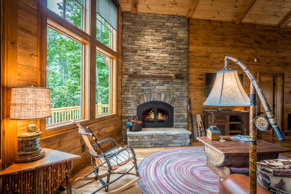 This is an example of a mid-sized country open concept family room in Charlotte with brown walls, medium hardwood floors, a standard fireplace, a stone fireplace surround, a wall-mounted tv and brown floor.