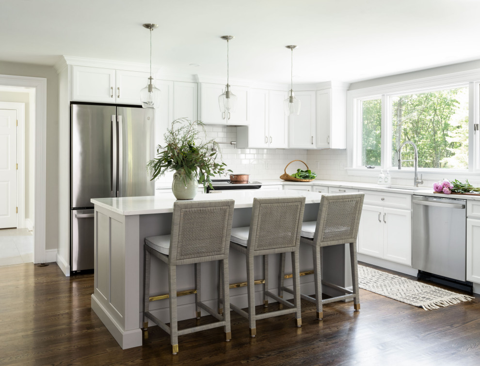 Klassisk inredning av ett vit vitt kök, med en undermonterad diskho, skåp i shakerstil, vita skåp, bänkskiva i kvarts, vitt stänkskydd, stänkskydd i keramik, rostfria vitvaror, mellanmörkt trägolv, en köksö och brunt golv
