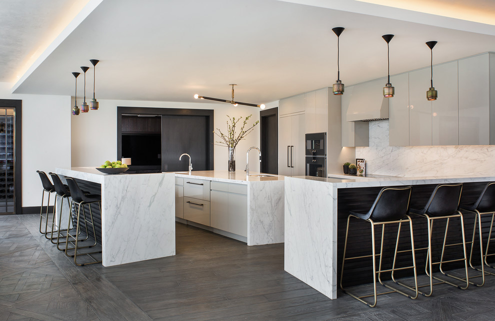 Design ideas for a contemporary kitchen in Los Angeles with an undermount sink, flat-panel cabinets, grey cabinets, white splashback, black appliances, dark hardwood floors, multiple islands and brown floor.