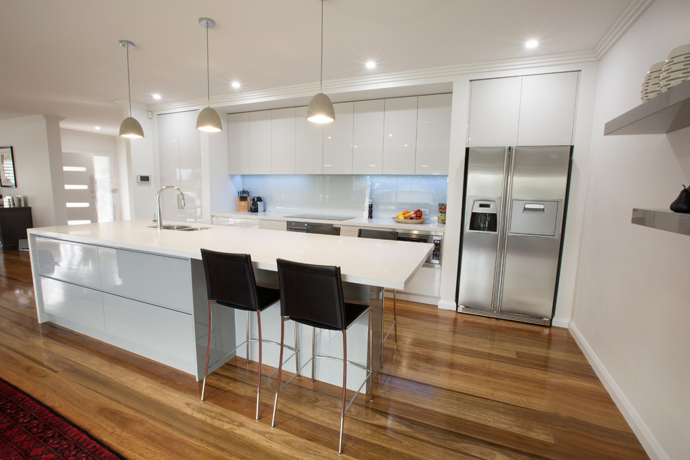 This is an example of a contemporary galley eat-in kitchen in Sydney with an undermount sink, flat-panel cabinets, grey cabinets, quartz benchtops, grey splashback, glass sheet splashback, stainless steel appliances, medium hardwood floors and with island.