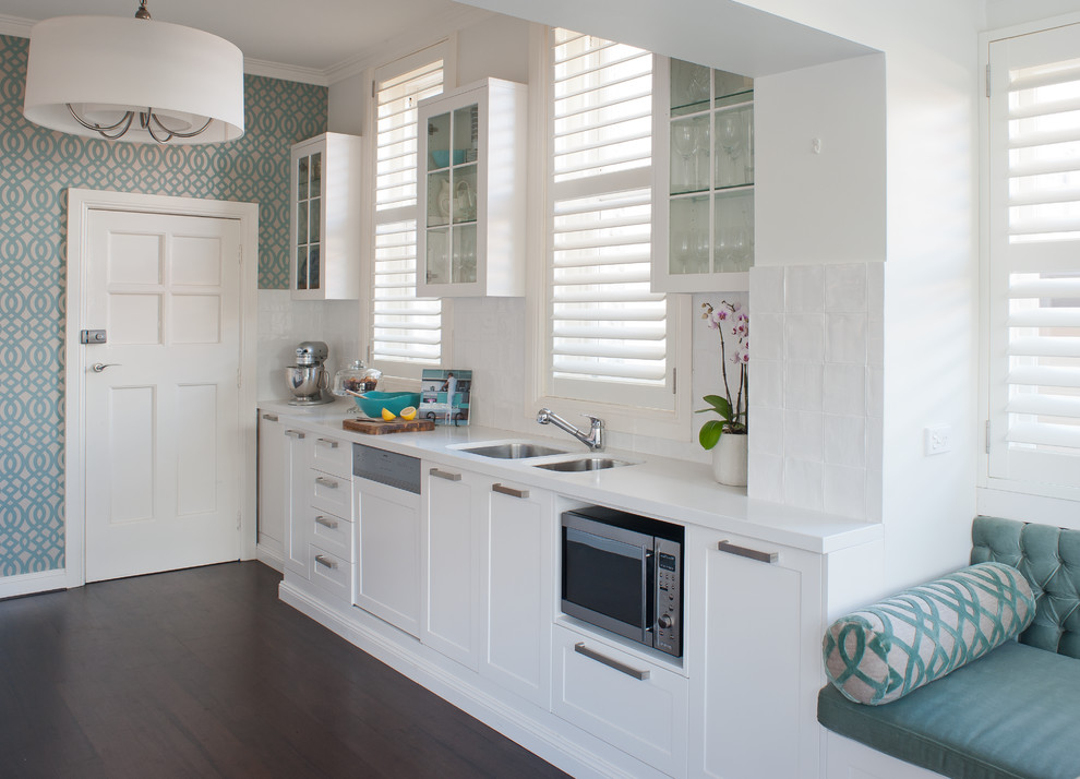 Design ideas for a mid-sized transitional galley eat-in kitchen in Sydney with an undermount sink, shaker cabinets, white cabinets, quartz benchtops, white splashback, porcelain splashback, stainless steel appliances, dark hardwood floors, no island and brown floor.