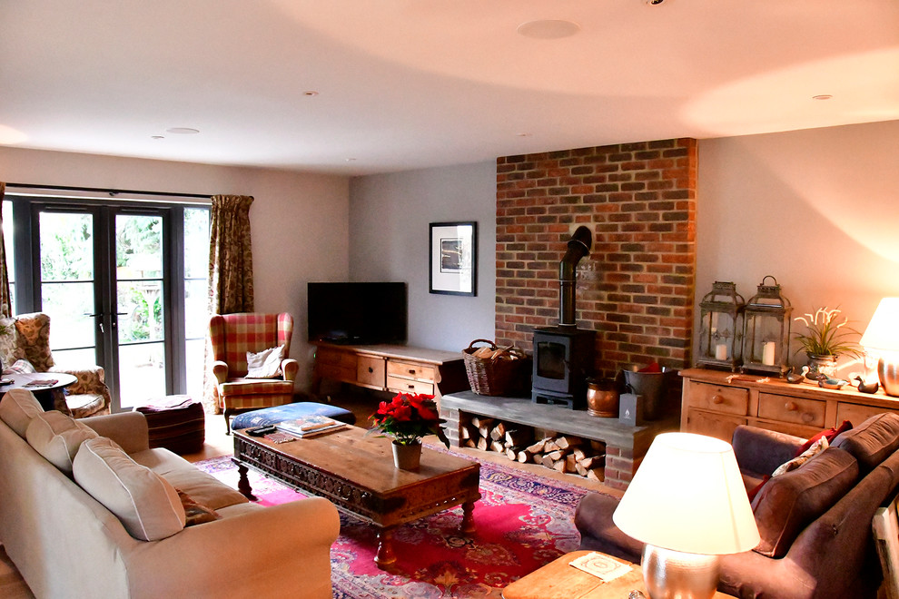This is an example of a large midcentury formal enclosed living room in Hertfordshire with grey walls, medium hardwood floors, a wood stove, a brick fireplace surround, a freestanding tv and beige floor.