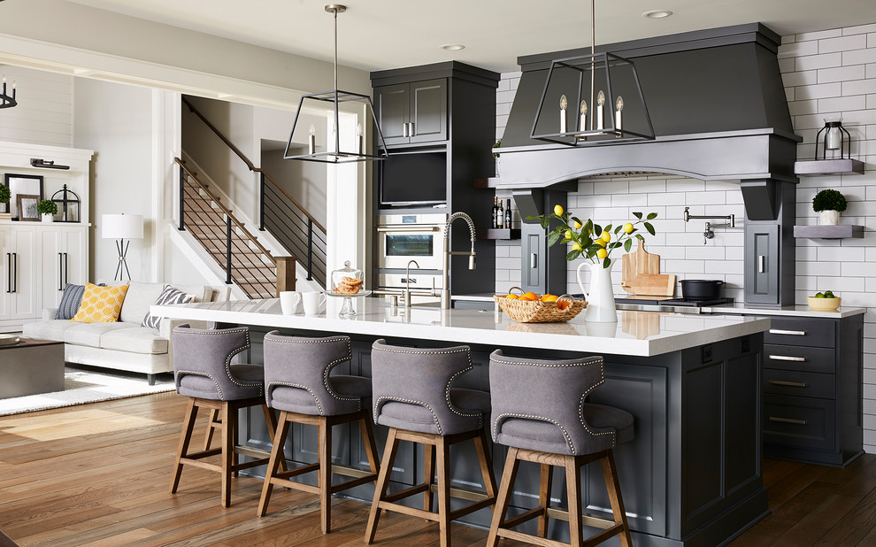 Inspiration for a large transitional l-shaped open plan kitchen in Minneapolis with an undermount sink, shaker cabinets, black cabinets, quartz benchtops, white splashback, subway tile splashback, stainless steel appliances, medium hardwood floors, with island, brown floor and white benchtop.