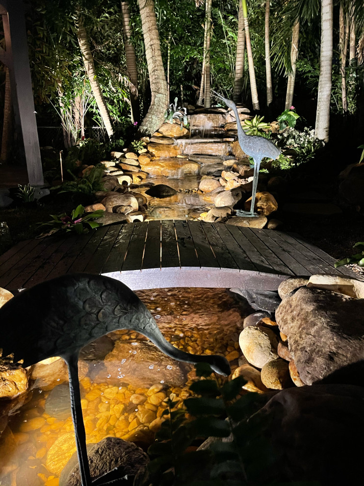 This is an example of a large asian backyard partial sun garden in San Diego with a garden path, with pond, with privacy feature, with rock feature, with path, with waterfall and natural stone pavers.
