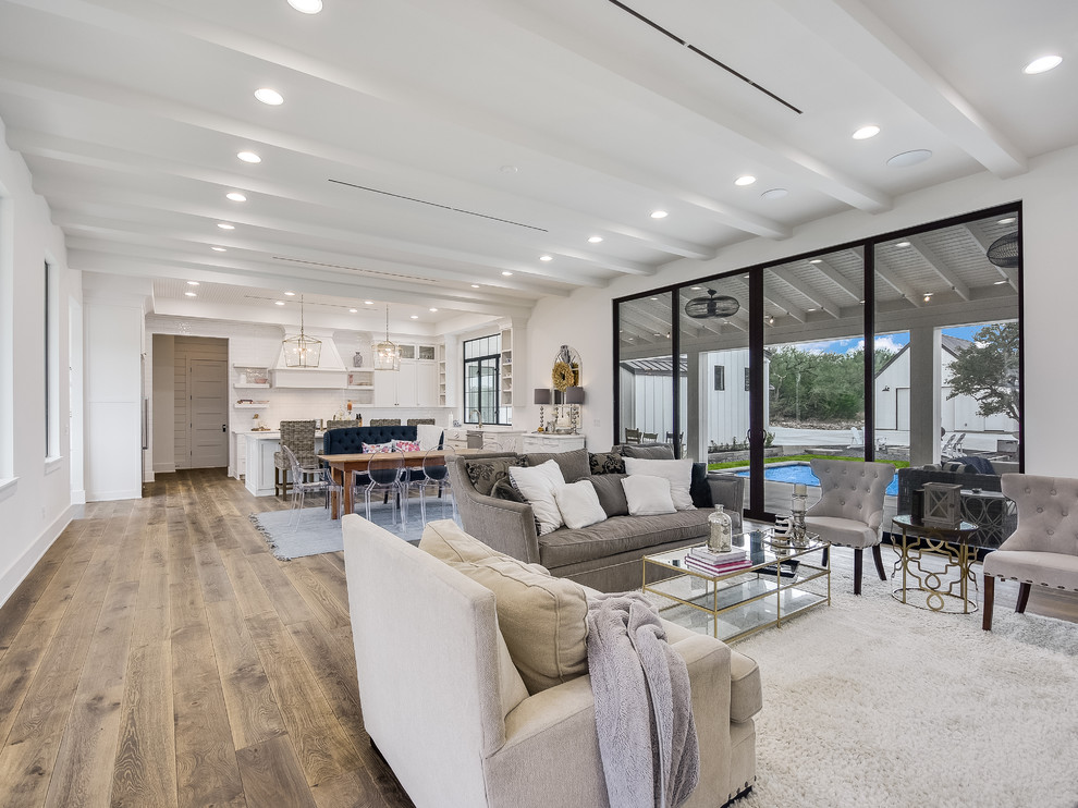 Photo of a large country formal open concept living room in Austin with white walls, light hardwood floors, no fireplace, a wall-mounted tv and grey floor.