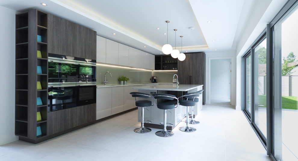 Photo of a mid-sized contemporary l-shaped open plan kitchen in London with an integrated sink, flat-panel cabinets, beige cabinets, solid surface benchtops, beige splashback, glass sheet splashback, stainless steel appliances and with island.