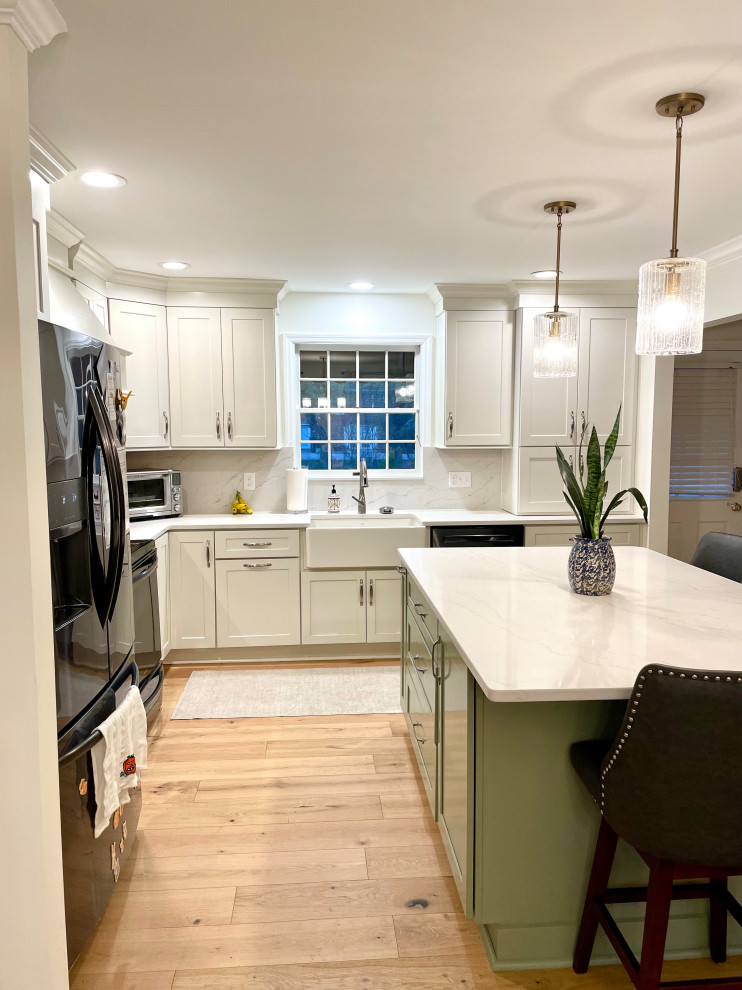 Example of a transitional l-shaped light wood floor and beige floor eat-in kitchen design with a farmhouse sink, shaker cabinets, white cabinets, quartz countertops, white backsplash, quartz backsplash, black appliances, an island and white countertops