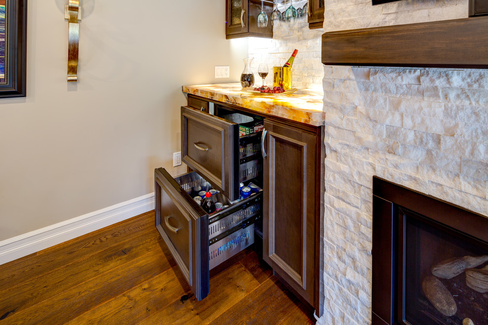 Small transitional single-wall home bar in Edmonton with no sink, glass-front cabinets, brown cabinets, white splashback, stone tile splashback, medium hardwood floors, brown floor, multi-coloured benchtop and onyx benchtops.