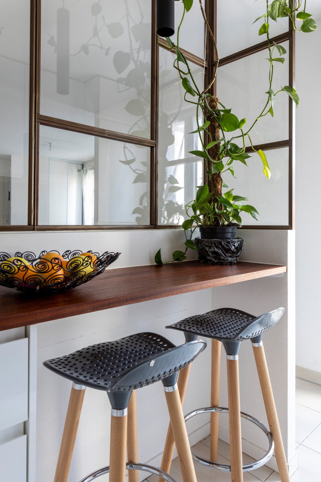パリにある低価格の小さなコンテンポラリースタイルのおしゃれなキッチン (一体型シンク、フラットパネル扉のキャビネット、白いキャビネット、木材カウンター、黒いキッチンパネル、セラミックタイルのキッチンパネル、シルバーの調理設備、セラミックタイルの床、ベージュの床、茶色いキッチンカウンター) の写真