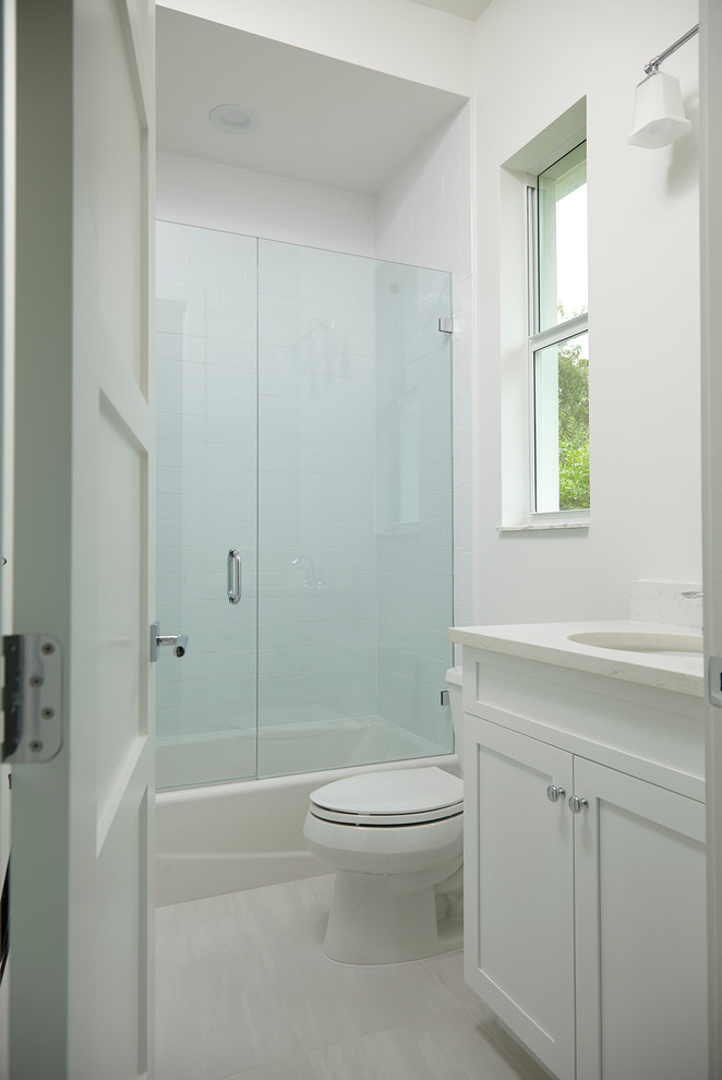 Inspiration for a mid-sized transitional bathroom in Miami with shaker cabinets, white cabinets, an alcove shower, a two-piece toilet, gray tile, porcelain tile, white walls, porcelain floors, an undermount sink and engineered quartz benchtops.