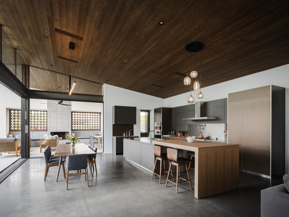 Inspiration for a modern l-shaped open plan kitchen in Phoenix with an integrated sink, flat-panel cabinets, black cabinets, stainless steel worktops, stainless steel appliances, concrete flooring, an island and a wood ceiling.