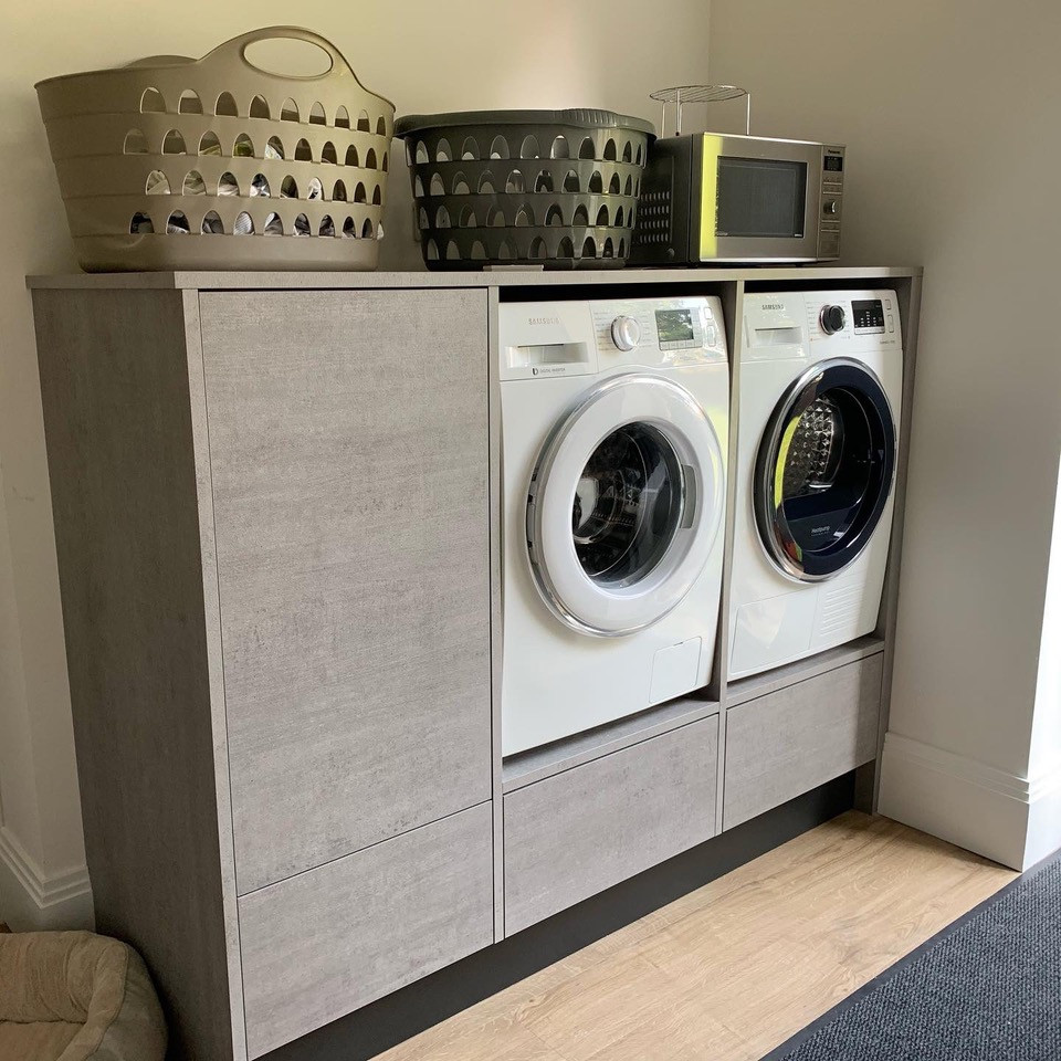 Imagen de lavadero pequeño con puertas de armario grises, lavadora y secadora juntas y suelo marrón