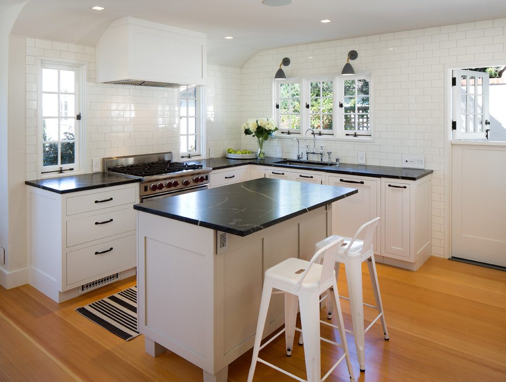 Inspiration for a mid-sized transitional l-shaped kitchen in San Diego with a single-bowl sink, shaker cabinets, white cabinets, soapstone benchtops, white splashback, subway tile splashback, medium hardwood floors, with island and stainless steel appliances.