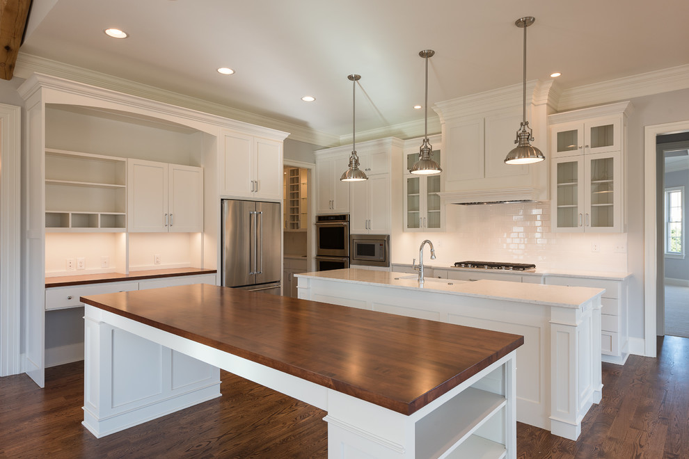 Example of a mid-sized transitional l-shaped dark wood floor and brown floor open concept kitchen design with a farmhouse sink, shaker cabinets, white cabinets, granite countertops, stainless steel appliances and two islands