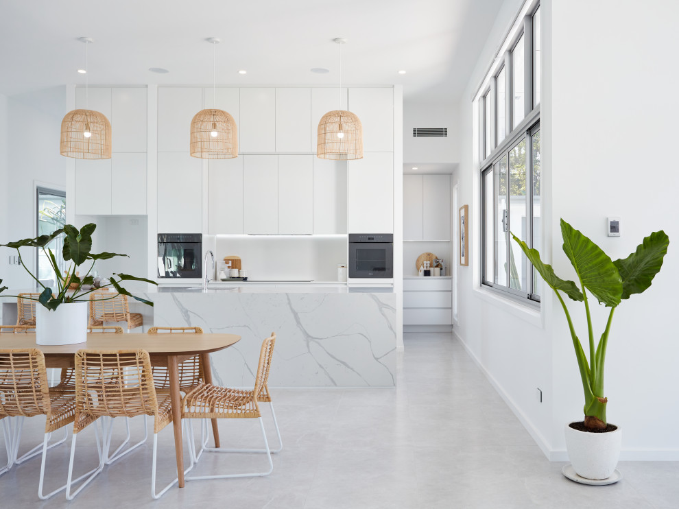 Contemporary u-shaped eat-in kitchen in Gold Coast - Tweed with flat-panel cabinets, white cabinets, white splashback, black appliances, with island, grey floor and grey benchtop.
