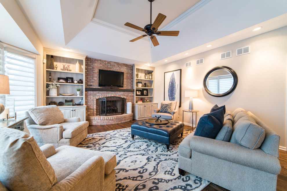 Photo of a mid-sized traditional family room in Chicago with white walls, a standard fireplace, a brick fireplace surround, a wall-mounted tv, brown floor and dark hardwood floors.