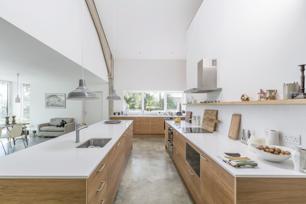 Example of a large farmhouse concrete floor and gray floor open concept kitchen design in Hertfordshire with flat-panel cabinets, medium tone wood cabinets, solid surface countertops, white backsplash, ceramic backsplash, paneled appliances, an island and white countertops