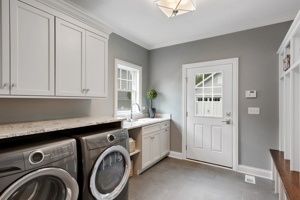 Inspiration for a mid-sized cottage single-wall porcelain tile, brown floor and brick wall dedicated laundry room remodel in Phoenix with an undermount sink, shaker cabinets, white cabinets, granite countertops, gray walls, a side-by-side washer/dryer and beige countertops