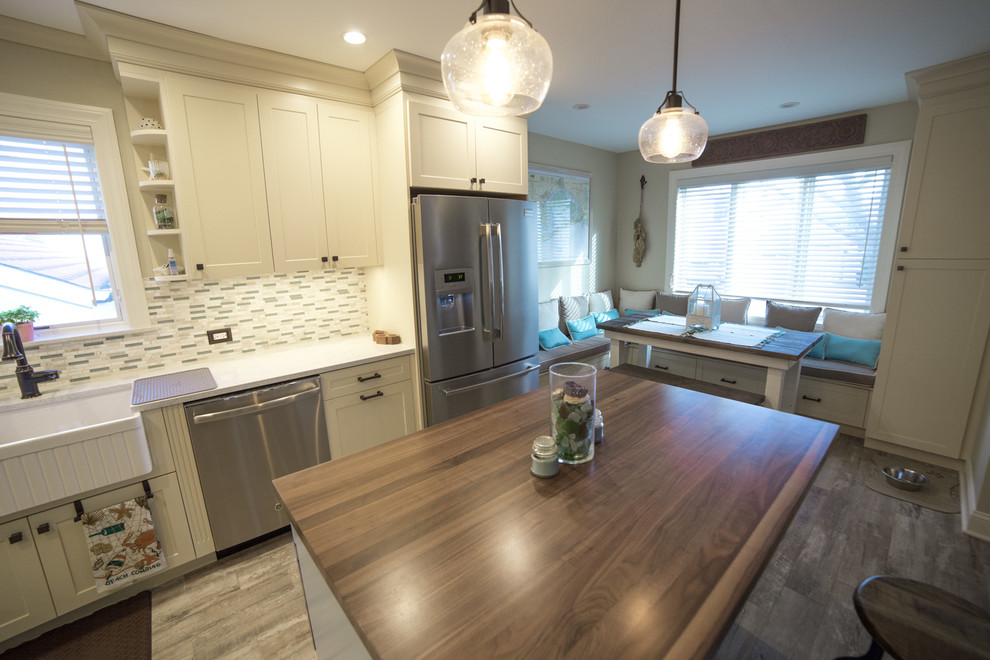 Mid-sized beach style l-shaped eat-in kitchen in New York with a farmhouse sink, shaker cabinets, yellow cabinets, quartz benchtops, green splashback, glass tile splashback, stainless steel appliances, porcelain floors and with island.