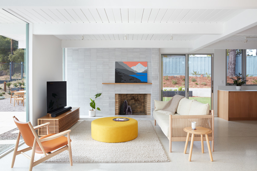This is an example of a midcentury family room in San Francisco with grey walls, a standard fireplace, a brick fireplace surround, a freestanding tv, white floor, timber and brick walls.