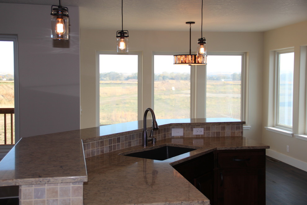 Example of a mountain style dark wood floor home design design with shaker cabinets, dark wood cabinets, beige backsplash, stainless steel appliances and an island