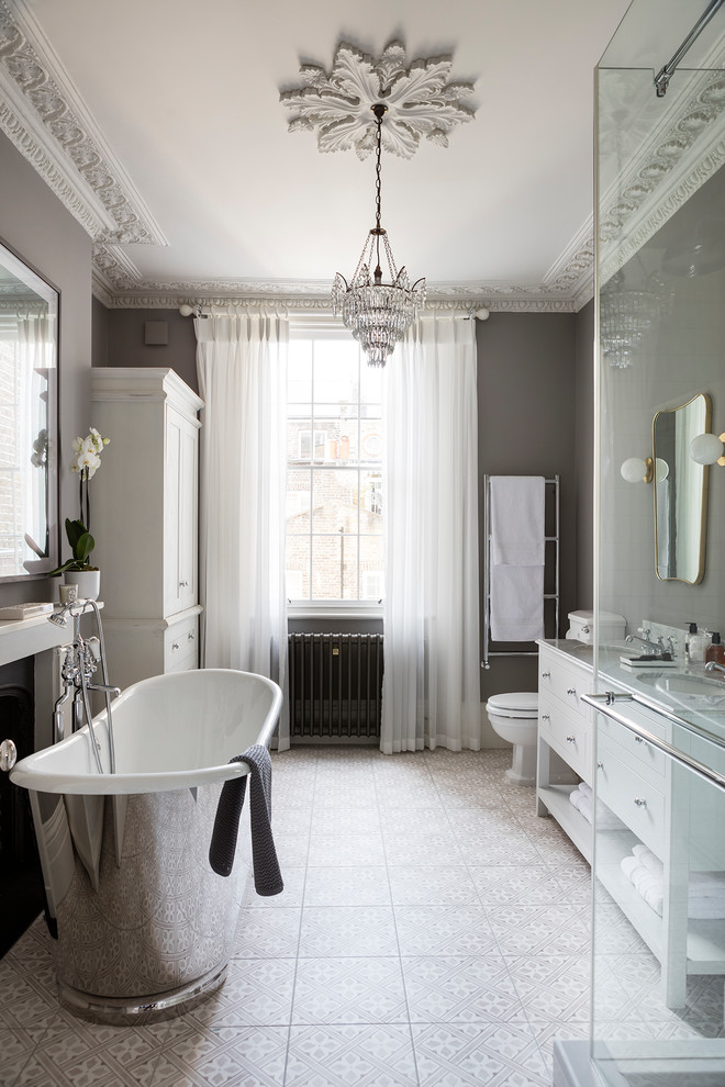 Large transitional bathroom in London with flat-panel cabinets, white cabinets, a freestanding tub, a corner shower, a one-piece toilet, grey walls, ceramic floors, a console sink, marble benchtops and grey floor.