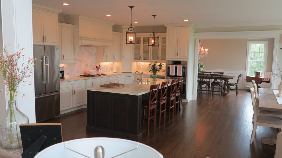 This is an example of a large traditional l-shaped eat-in kitchen in Bridgeport with a farmhouse sink, raised-panel cabinets, white cabinets, marble benchtops, white splashback, marble splashback, stainless steel appliances, dark hardwood floors, with island, brown floor and white benchtop.