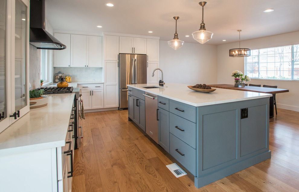 This is an example of a mid-sized contemporary galley eat-in kitchen in Denver with an undermount sink, glass-front cabinets, beige cabinets, quartz benchtops, white splashback, ceramic splashback, stainless steel appliances, medium hardwood floors and with island.