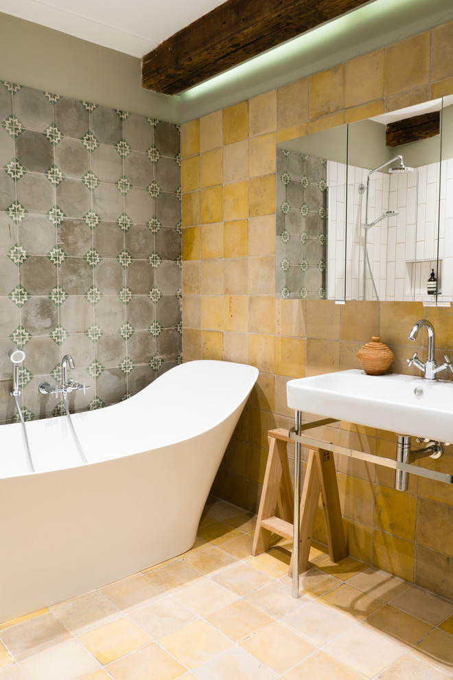 Mid-sized eclectic bathroom in London with a freestanding tub, gray tile, yellow tile, ceramic tile, ceramic floors, a wall-mount sink and yellow floor.