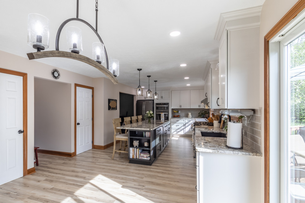 Photo of a large contemporary l-shaped eat-in kitchen in Cleveland with an undermount sink, shaker cabinets, white cabinets, granite benchtops, beige splashback, subway tile splashback, stainless steel appliances, vinyl floors, with island, beige floor and grey benchtop.
