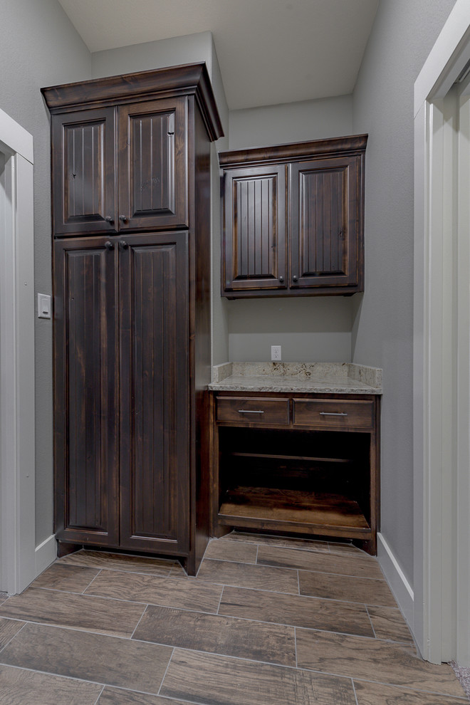 Small industrial galley utility room in Other with an utility sink, raised-panel cabinets, dark wood cabinets, granite benchtops, grey walls, ceramic floors, a side-by-side washer and dryer and brown floor.