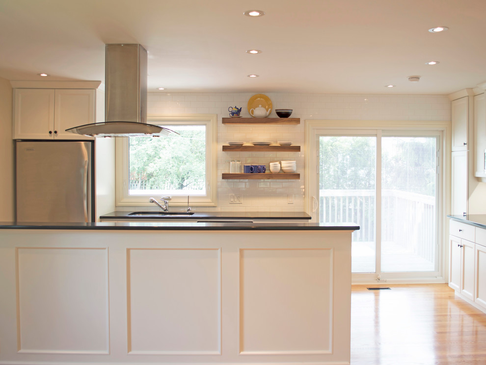 Open concept kitchen - mid-sized transitional galley light wood floor open concept kitchen idea with an undermount sink, shaker cabinets, white cabinets, quartzite countertops, white backsplash, subway tile backsplash, stainless steel appliances, a peninsula and black countertops