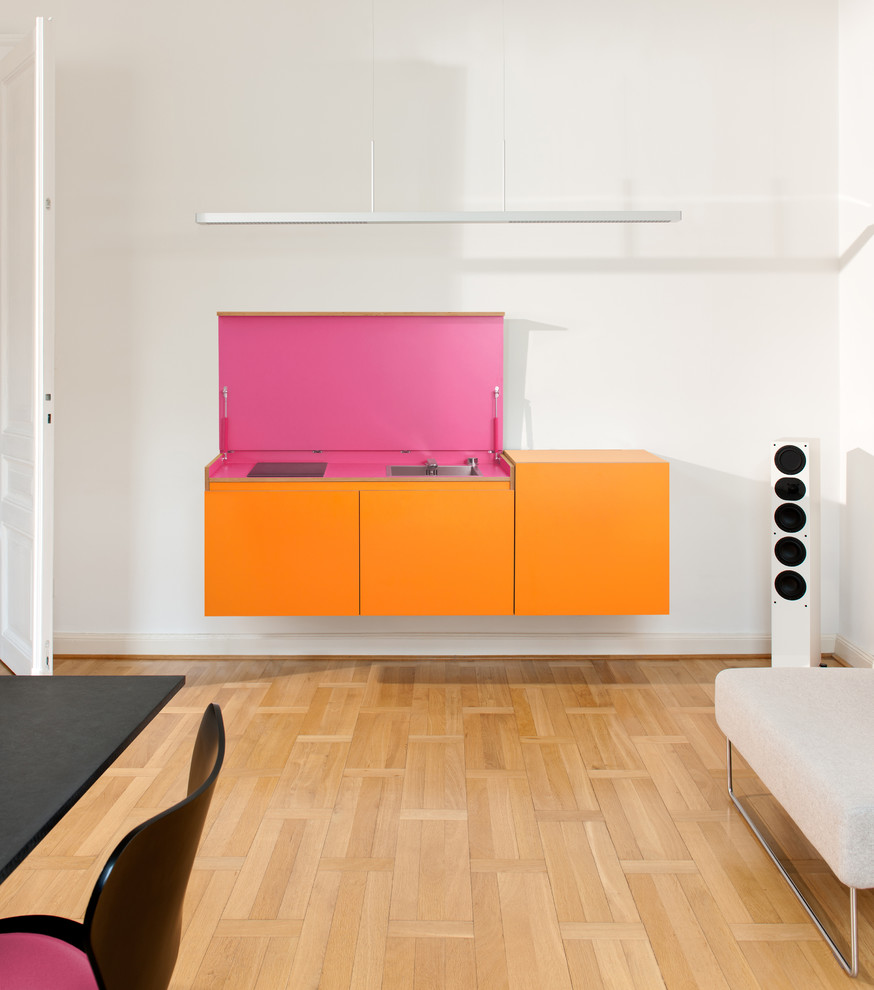 Photo of a small contemporary single-wall eat-in kitchen in Dusseldorf with a drop-in sink, orange cabinets, white splashback, no island, medium hardwood floors and brown floor.