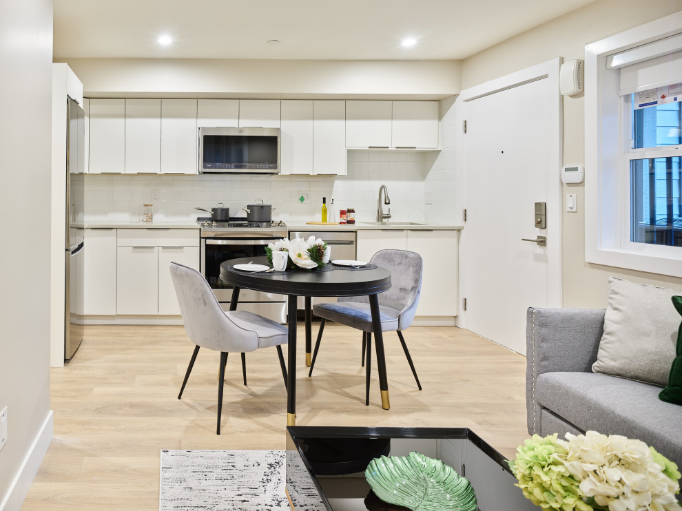 Eat-in kitchen - small transitional single-wall laminate floor and beige floor eat-in kitchen idea in Vancouver with an undermount sink, flat-panel cabinets, white cabinets, quartzite countertops, white backsplash, ceramic backsplash, stainless steel appliances, an island and beige countertops