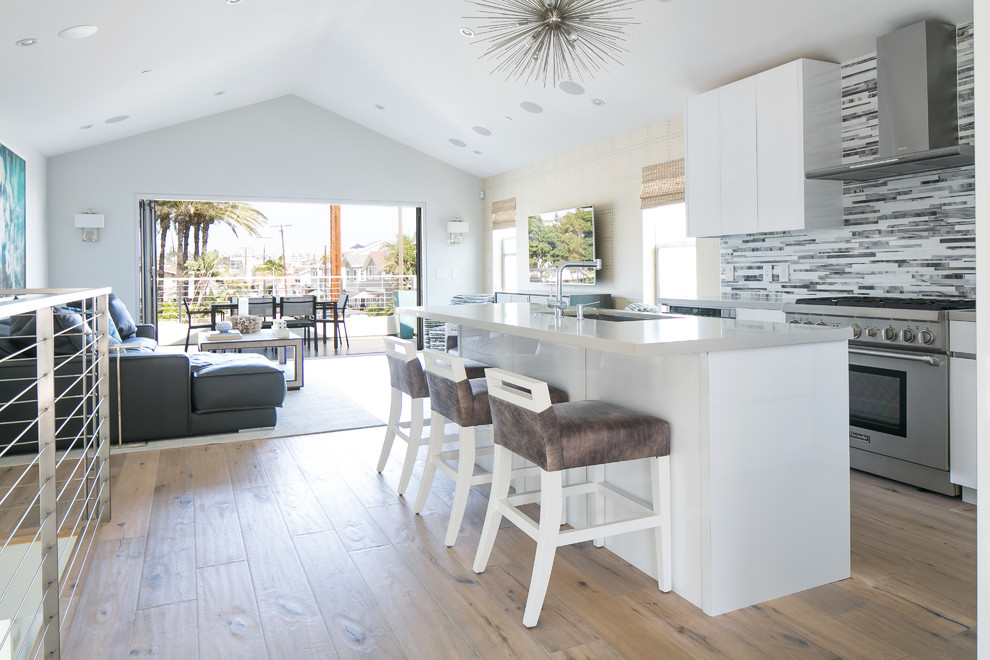 Photo of a beach style galley open plan kitchen in Orange County with an undermount sink, flat-panel cabinets, white cabinets, stainless steel appliances, medium hardwood floors, with island and multi-coloured splashback.