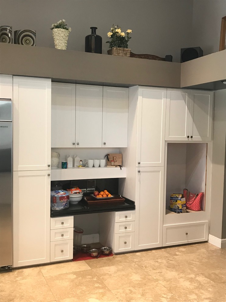 Photo of a large transitional l-shaped kitchen pantry in Miami with shaker cabinets, white cabinets, a peninsula, black splashback, stainless steel appliances, ceramic floors and brown floor.