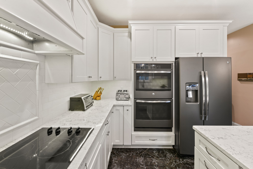 This is an example of a mid-sized modern u-shaped eat-in kitchen in Jacksonville with a farmhouse sink, shaker cabinets, white cabinets, quartzite benchtops, white splashback, subway tile splashback, coloured appliances, porcelain floors, with island and black floor.