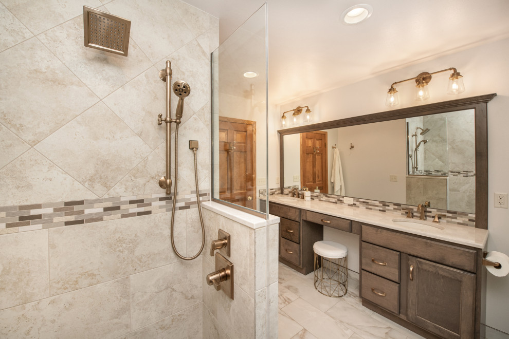This is an example of a large traditional ensuite bathroom in Milwaukee with recessed-panel cabinets, medium wood cabinets, an alcove shower, a two-piece toilet, beige tiles, porcelain tiles, white walls, porcelain flooring, a submerged sink, engineered stone worktops, beige floors, a hinged door, beige worktops, a shower bench, double sinks and a built in vanity unit.