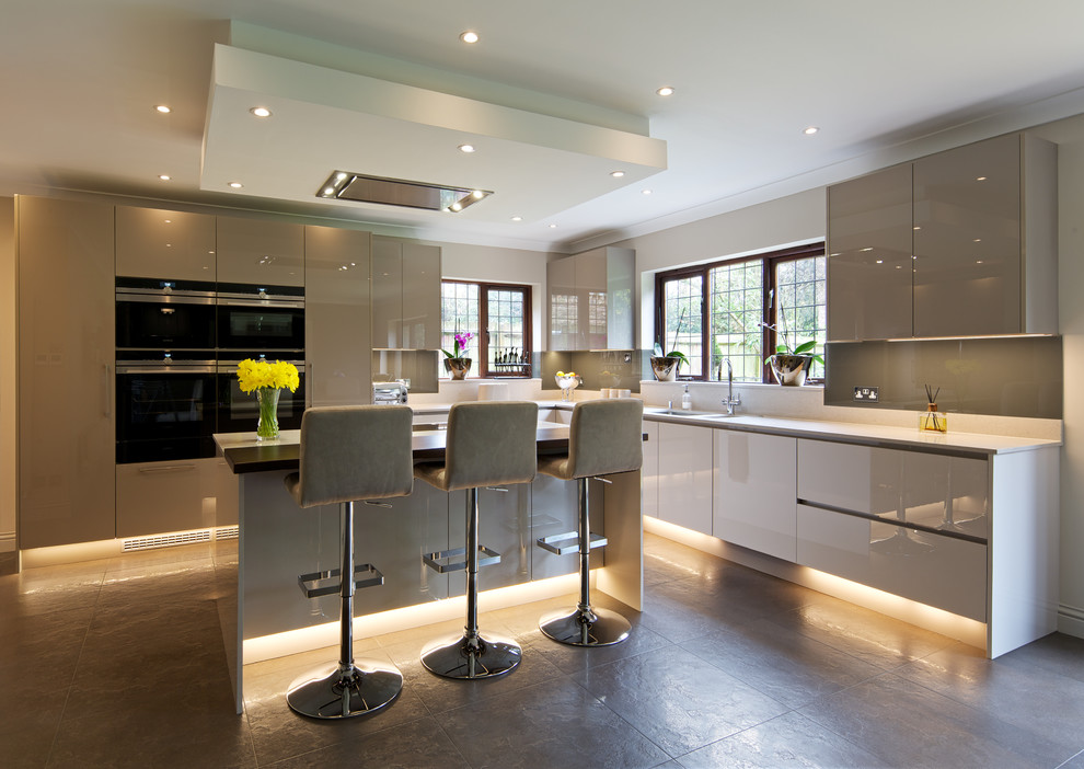 Large contemporary l-shaped eat-in kitchen in Hertfordshire with an undermount sink, flat-panel cabinets, grey cabinets, quartzite benchtops, grey splashback, glass tile splashback, black appliances, porcelain floors, with island and grey floor.