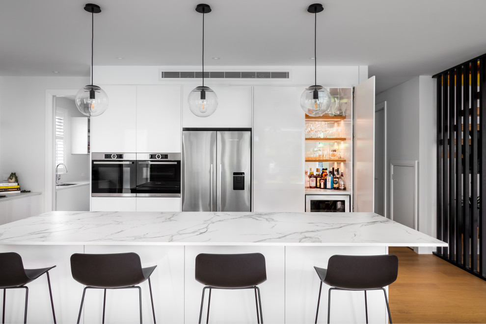 Large contemporary l-shaped eat-in kitchen in Auckland with an undermount sink, recessed-panel cabinets, white cabinets, quartz benchtops, white splashback, porcelain splashback, stainless steel appliances, light hardwood floors, with island and yellow benchtop.