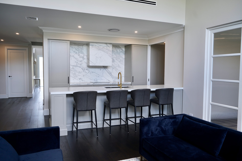 Inspiration for a large transitional single-wall open plan kitchen in Sydney with an undermount sink, shaker cabinets, grey cabinets, marble benchtops, white splashback, marble splashback, black appliances, dark hardwood floors, with island, brown floor and white benchtop.